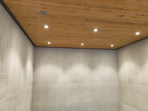Photo of a cubicle-like architectural space consisting od white stone walls and wooden ceiling with lighting
