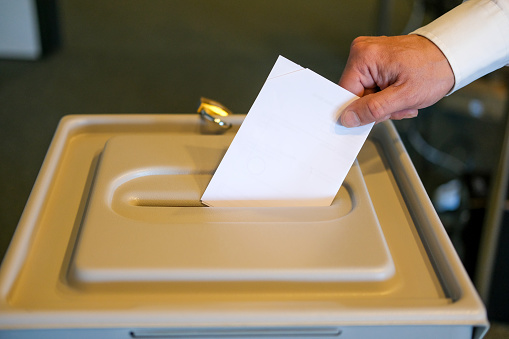 Close-up of a man's hand putting his ballot into the ballot box, with plenty of copy space, selective focus