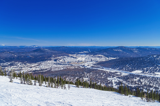 View from mount Green of Sheregesh village, snow ski slopes, beautiful panorama with range mountains and hills far away, fir trees forest, clear blue sky, picturesque winter nature, sunny weather.
