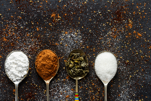 Spoons with icing sugar, green tea and cocoa on black background sprinkled with brown and white sugar, coffee, cocoa powder.