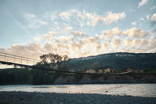 Mountain landscape at sunset. Suspension bridge over a mountain river. Wooden houses away