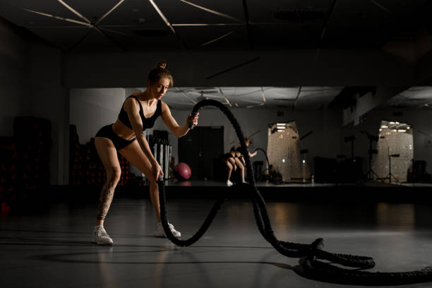 istock Attractive young fit sportswoman working out in functional training gym doing battle ropes exercise 1894748862