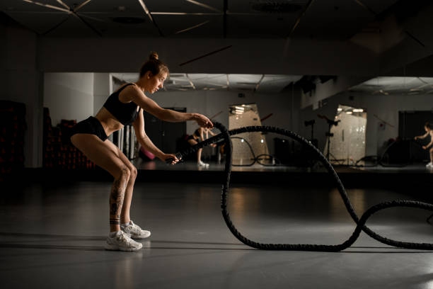 istock Attractive young fit sportswoman working out in functional training gym doing gym exercise with battle ropes against mirror 1894748874