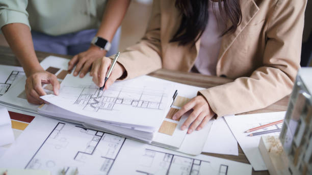 istock Two female architects discussing about interior designing building project and drawing on blueprint 1894752354