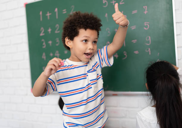 happy african american kid boy studying and writing with chalkboard and friend in classroom - child group of people multi ethnic group classroom ストックフォトと画像
