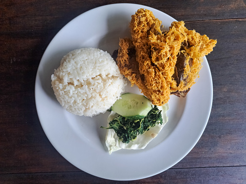 Serving Food Of Nasi Ayam Goreng Kremes Or Crispy Fried Chicken With Rice, Crispy Spiced Flakes, Rice, Cucumber Sliced, Cabbage And Boiled Cassava Leaves. Dinner Menu. Top View