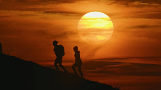 istock Side View of Silhouette Couple Climbing Mountain against Dramatic Sky During Sunset 1894766423