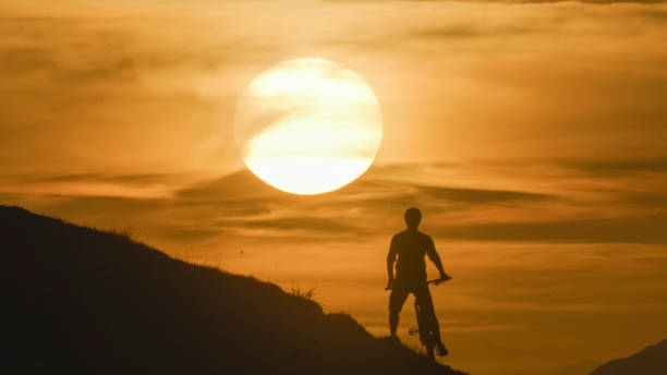 istock Rear View of Silhouette Mountain Biker Standing with Bicycle on Hill against Dramatic Orange Sky during Sunset 1894766448
