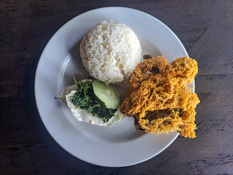 Tasty Nasi Ayam Goreng Kremes Or Crispy Fried Chicken With Rice, Crispy Spiced Flakes, Rice, Cucumber Sliced, Cabbage And Boiled Cassava Leaves. Food Menu. Top View.