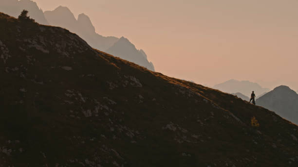 istock Distant View of Mountain Biker Standing on Hill against Clear Sky during Sunset 1894766986
