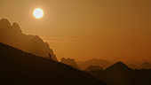 Distant View of Silhouette Mountain Biker Cycling Uphill against Mountain Range and Orange Sunset Sky
