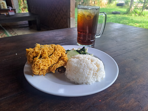Serving Of Nasi Ayam Goreng Kremes Or Crispy Fried Chicken With Rice, Crispy Spiced Flakes, Rice, Cucumber Sliced, Cabbage, Boiled Cassava Leaves And Fresh Tea Iced Or Es Teh Segar. Food And Drink Menu.