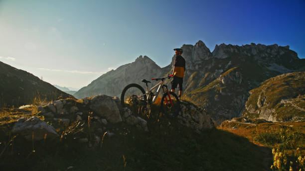 istock Rear View of Male Biker Standing with Bicycle on Rocky Hill against Mountain Range during Sunny Day 1894775430