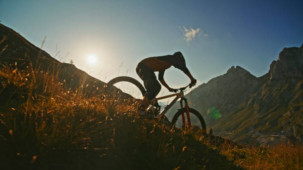 istock Determined Mountain Biker Cycling on Grassy Hill against Blue Sky during Sunny Day 1894775439