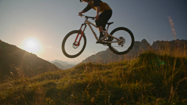 istock Mountain Biker Performing Stunt with Bicycle on Grassy Field against Bright Clear Sky during Sunset 1894775970