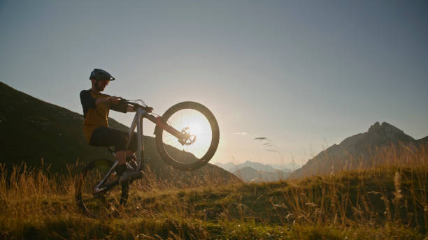 istock Determined Mountain Biker Performing Stunt with Bicycle on Grassy Field against Blue Sky during Sunset 1894775975