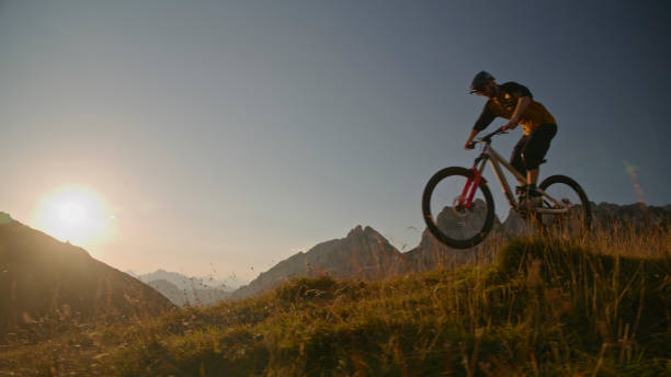 istock Low Angle View of Mountain Biker Performing Stunt with Bicycle on Grassy Field against Clear Sky during Sunset 1894775978