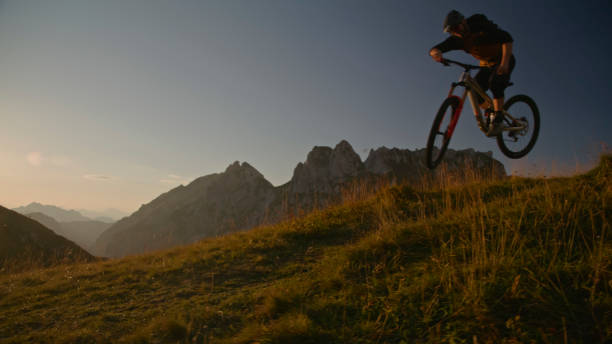 istock Mountain Biker Performing Stunt with Bicycle on Grassy Field against Clear Sky during Sunset 1894775997