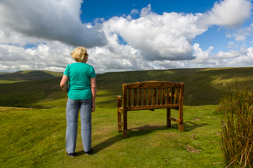 Rear view of a senior woman stood next to bench at a viewpoint in the Yorkshire Dales National Park, England.