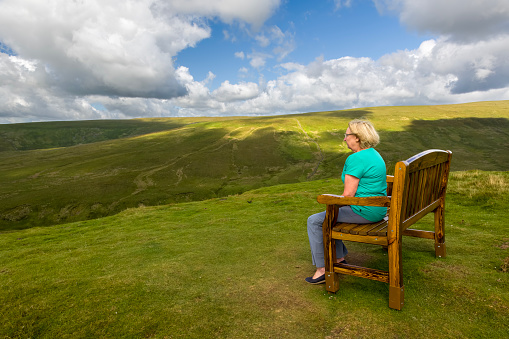 Side view of a senior woman sat on a bench at a viewpoint in the Yorkshire Dales National Park, England.