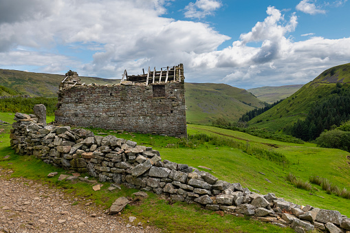 Damaged dry stone wall and derelict old barn in the rolling landscape of the southern area of the Yorkshire Dales National Park in England.