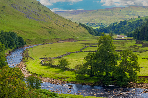 A river runs through the rolling landscape of the southern area of the Yorkshire Dales National Park in England.
