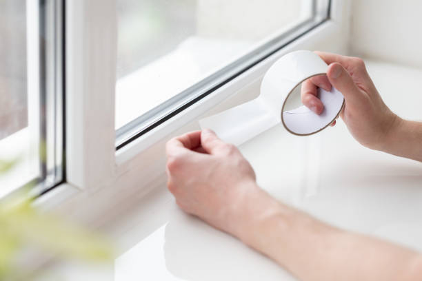 istock Man putting draught excluder tape on window, protection from the draft. 1894877989