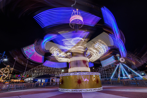 Neon illuminated carousel spinning fast in nighttime amusement park. Long exposure effect