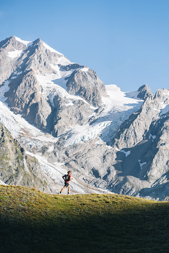 Distant view of trail runner bounding along mountain trail below glaciated peaks