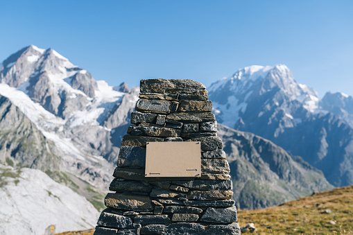 Rock cairn and plaque on mountain pass, snowcapped peaks behind