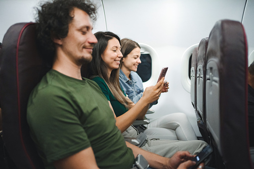 Three passengers using mobile phones on an airplane flight