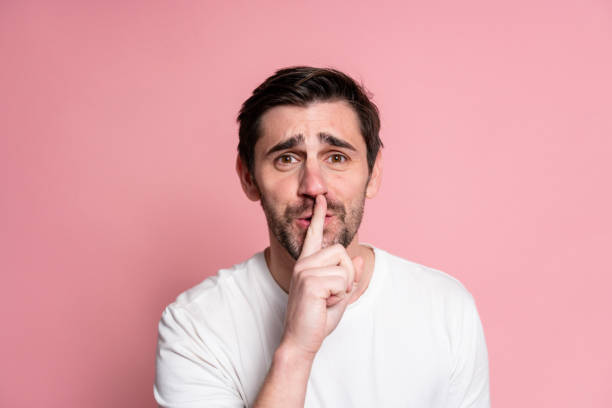 istock Portrait of a young man making silence gesture on a pink background 1894975193