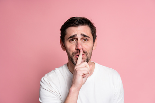 Portrait of a young man making silence gesture on a pink background