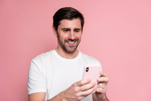 istock Portrait of a happy man using mobile phone while standing against pink background 1894975721