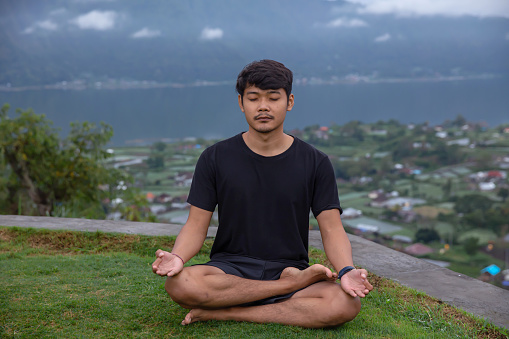 Close-up shot of Indonesian man with eyes closed, doing meditation and breathing exercise in the nature.