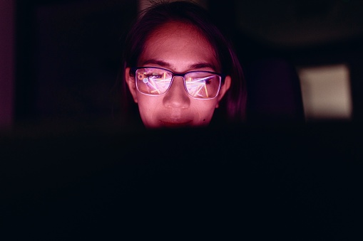 Beautiful woman with glasses working on a laptop at night