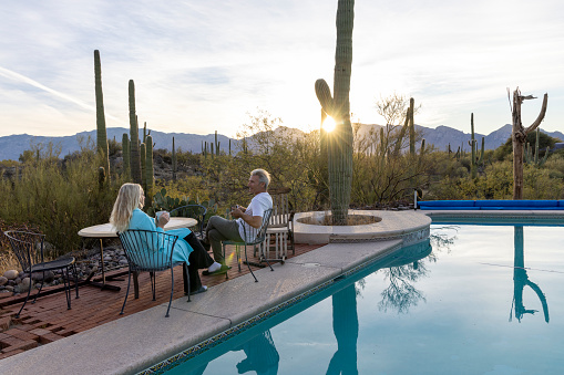 Mature couple relax by outdoor pool in desert at sunrise