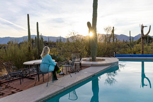 Mature woman relaxes by outdoor pool in desert at sunrise