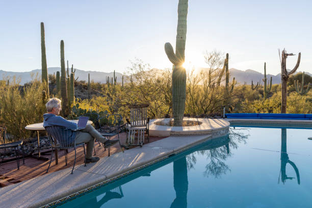istock Mature man uses laptop by outdoor pool 1895074136