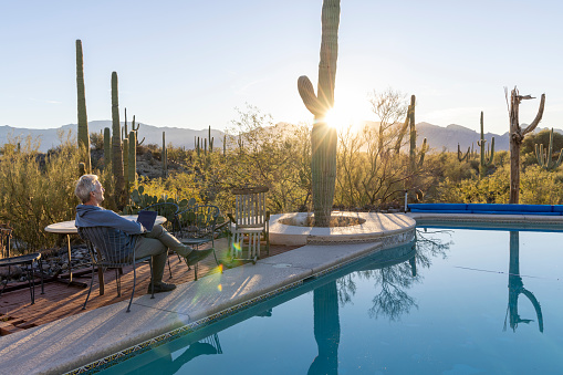 Mature man uses laptop by outdoor pool in desert at sunrise