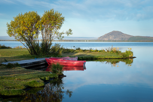 Small red rowing boat on calm water of Mývatn lake in Iceland in summer