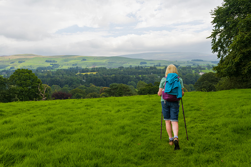 Rear view of an active senior hiker walking with poles on a footpath in the Yorkshire Dales National Park, England.