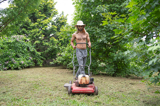 A man mows the grass with an electric lawn mower.Hardworking owner takes care of his lawn