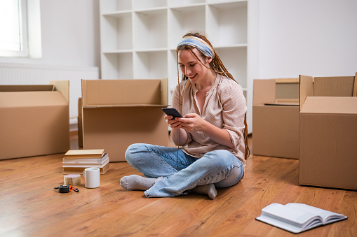 Modern ginger woman with braids using phone while moving into her new apartment.