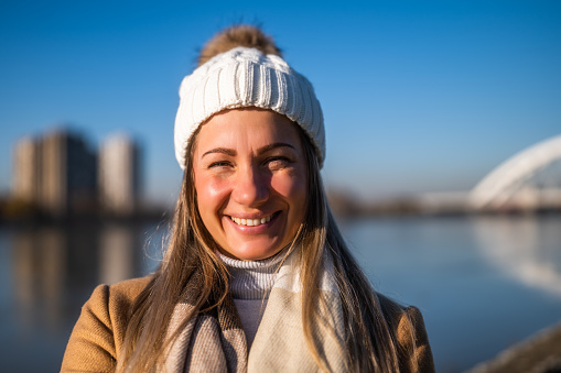 Close up of natural beautiful woman in warm clothing enjoys spending time by the river on a sunny winter day.