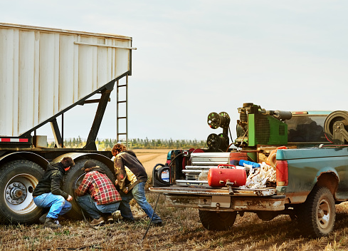 Group of three farm workers working as a team to repair the tyre of a grain box trailer on agricultural field