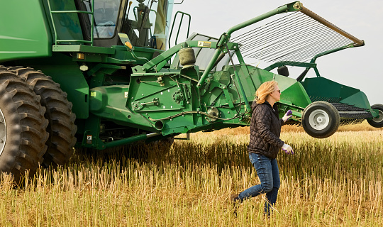 Mid adult female farmer walking to the front of combine harvester machine in a farm field