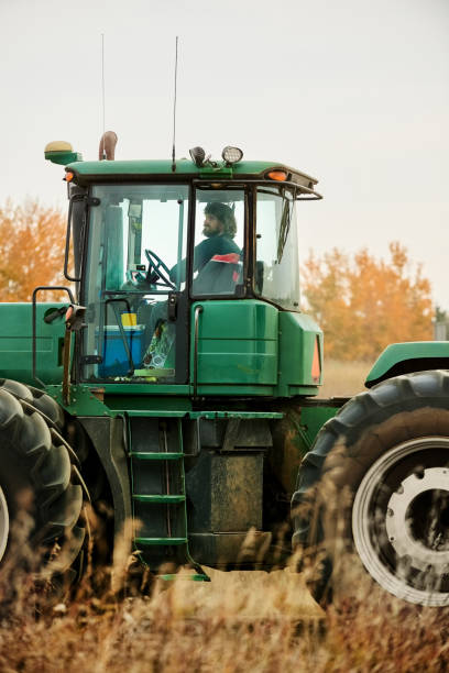 Side view of a male farmer driving a tractor on agricultural farm field