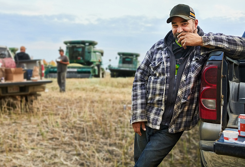 Portrait of a man standing by his pickup truck on farm field taking lunch break during harvest time