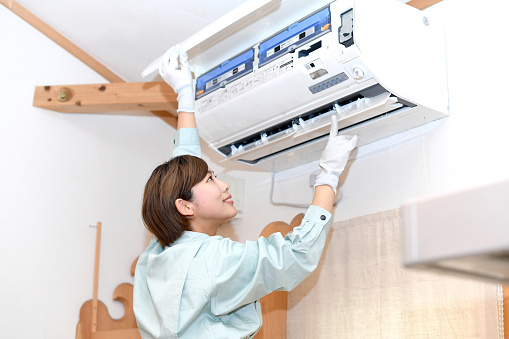 Asian woman wearing work clothes and checking the system air conditioner